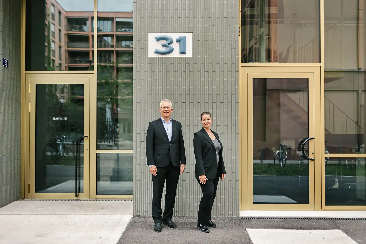 Das Foto zeigt Rolf Benz und Silvy Gillhausen, die vor ihrem neuen Büro in Winterthur-Neuhegi stehen. Der Bildlink führt auf die Seite Angebot.